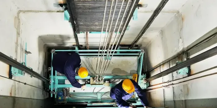 Hotel elevator maintenance technicians inspecting elevator shaft representing the critical equipment certifications and vendor contracts hotel management companies track in RenewAlert